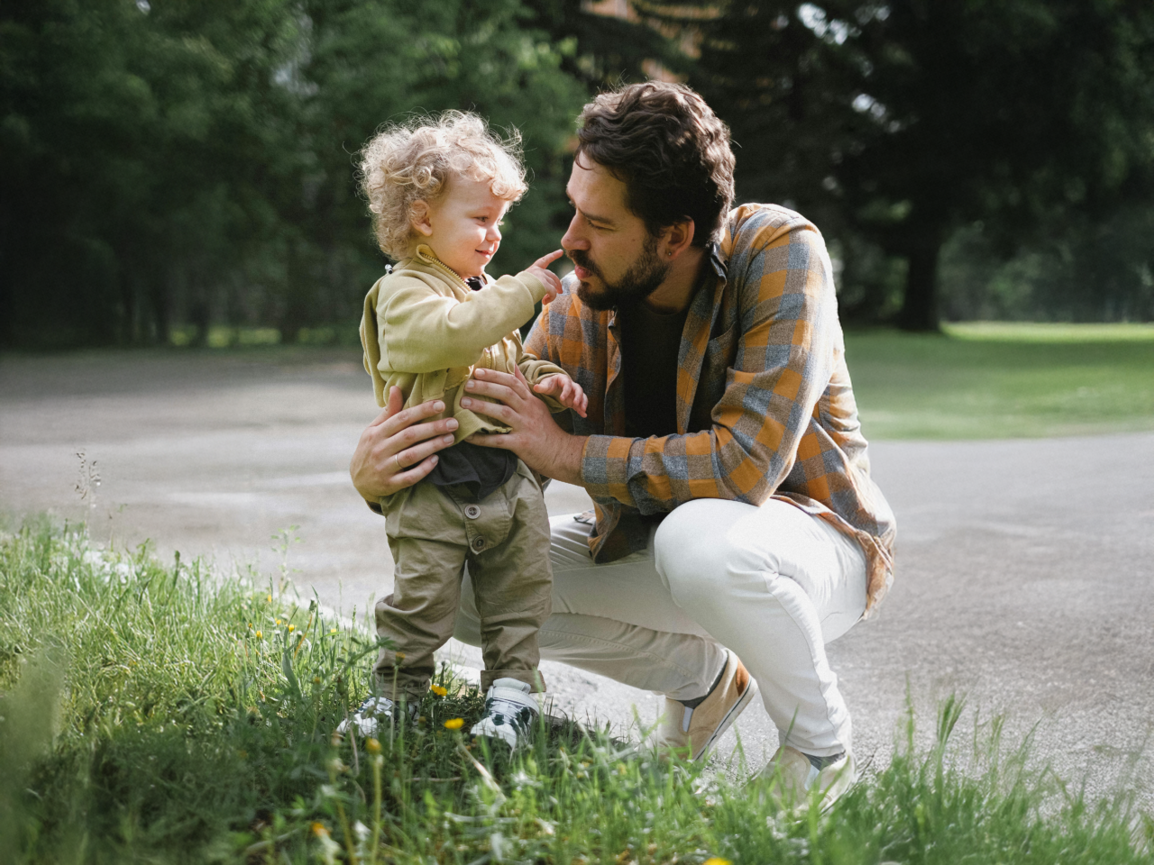 A father and child playing together in a grassy outdoor space.